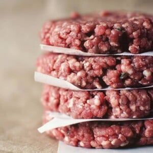 A stack of ground beef burgers on top of a piece of paper.