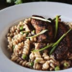 Blackened chicken mac and cheese in a white bowl garnished with scallions.