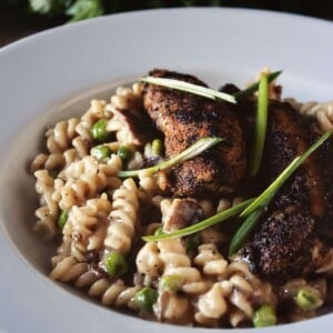Blackened chicken mac and cheese in a white bowl garnished with scallions.