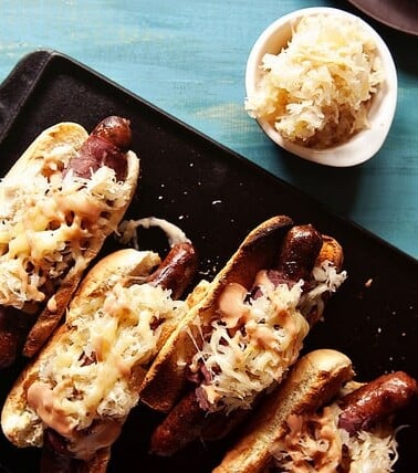 Reuben hot dog with sauerkraut and mustard on a tray.