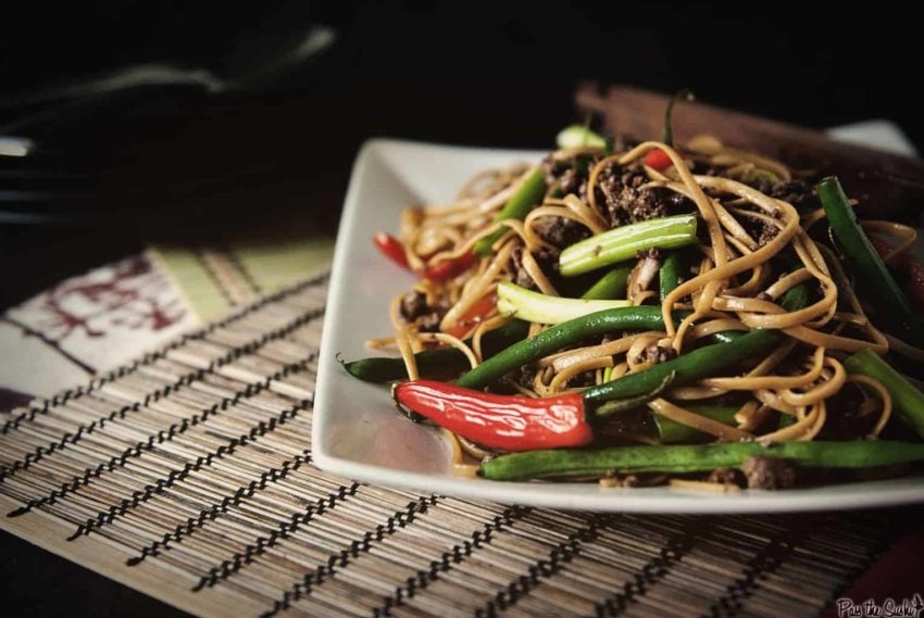 Szechuan noodles with vegetables and beef on a white plate