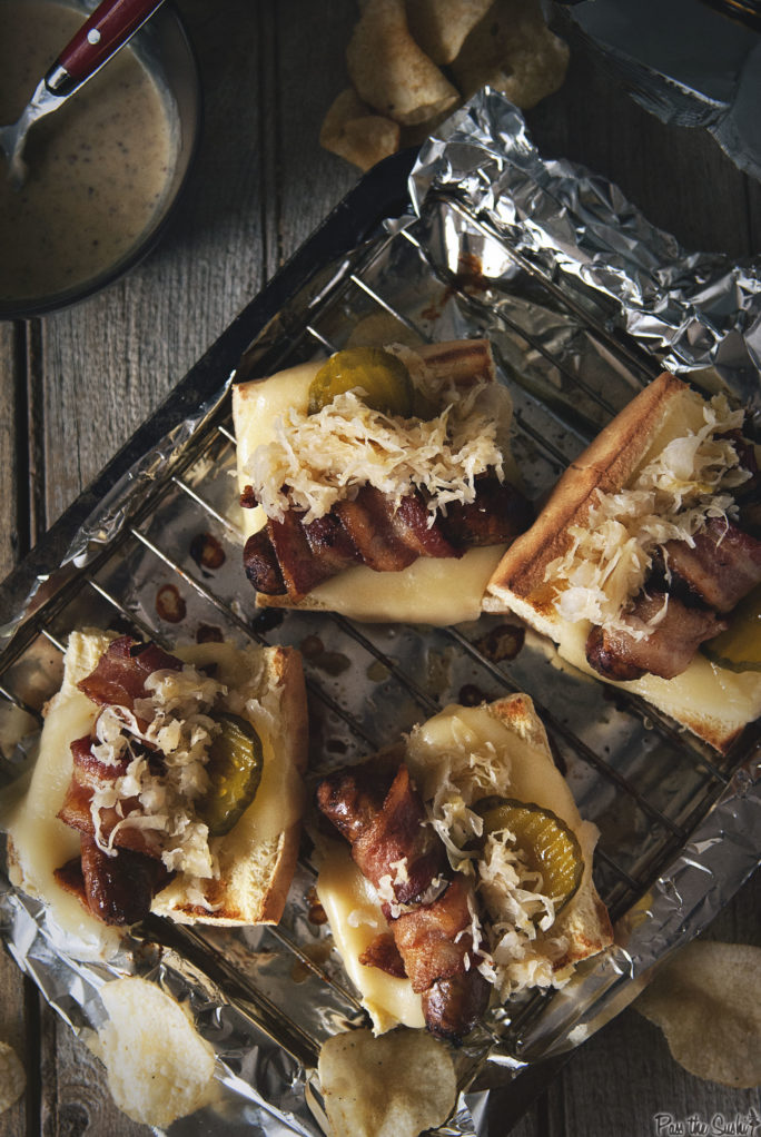 Bacon Wrapped Beer Brats on a tray with onions cheese and pickles.