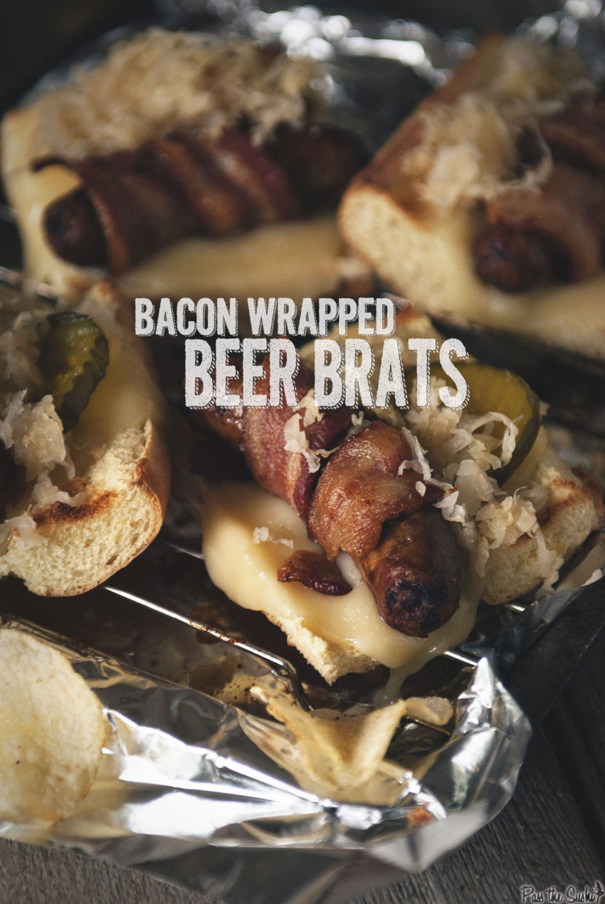 Bacon Wrapped Beer Brats on toasted bread with pickles and onion on aluminium foil and a side of chips