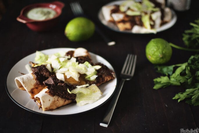 Two enchiladas just slathered with sauce and cheese and sprinkled with greens. Those limes in the background aren't just for show. Grab one and squeeze it on top!