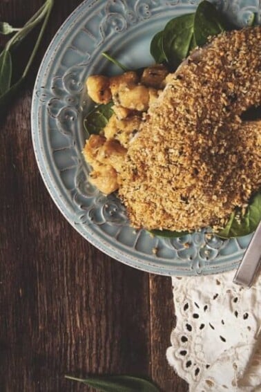 Baked tilapia fillets coated in a soft chickpea crust, served on a plate garnished with sage leaves.