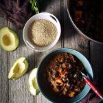 A bowl of quinoa chili with turkey and sweet potato stew on a wooden table.