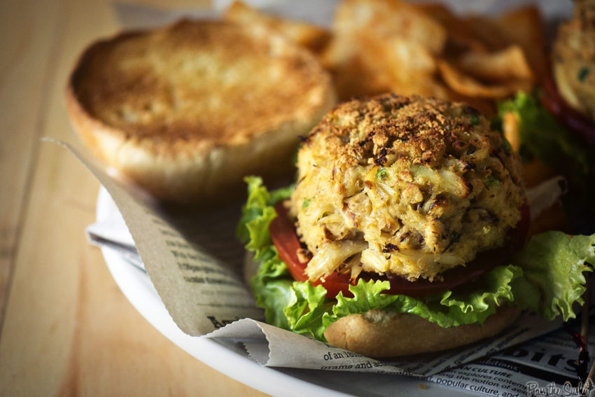 Authentic maryland crab cakes on a soft bun with lettuce and tomato slices, open faced. 