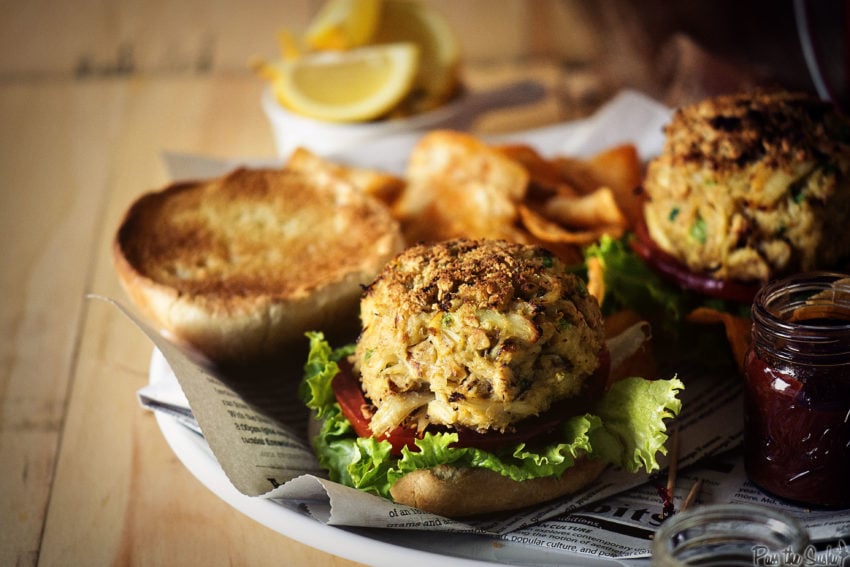 Two open face crab cake sandwiches with jumbo lump blue crab meat on buns, with lettuce tomato and chips.