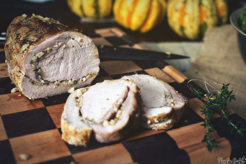 A garlic stuffed pork roast sliced on a cutting board with herbs. 