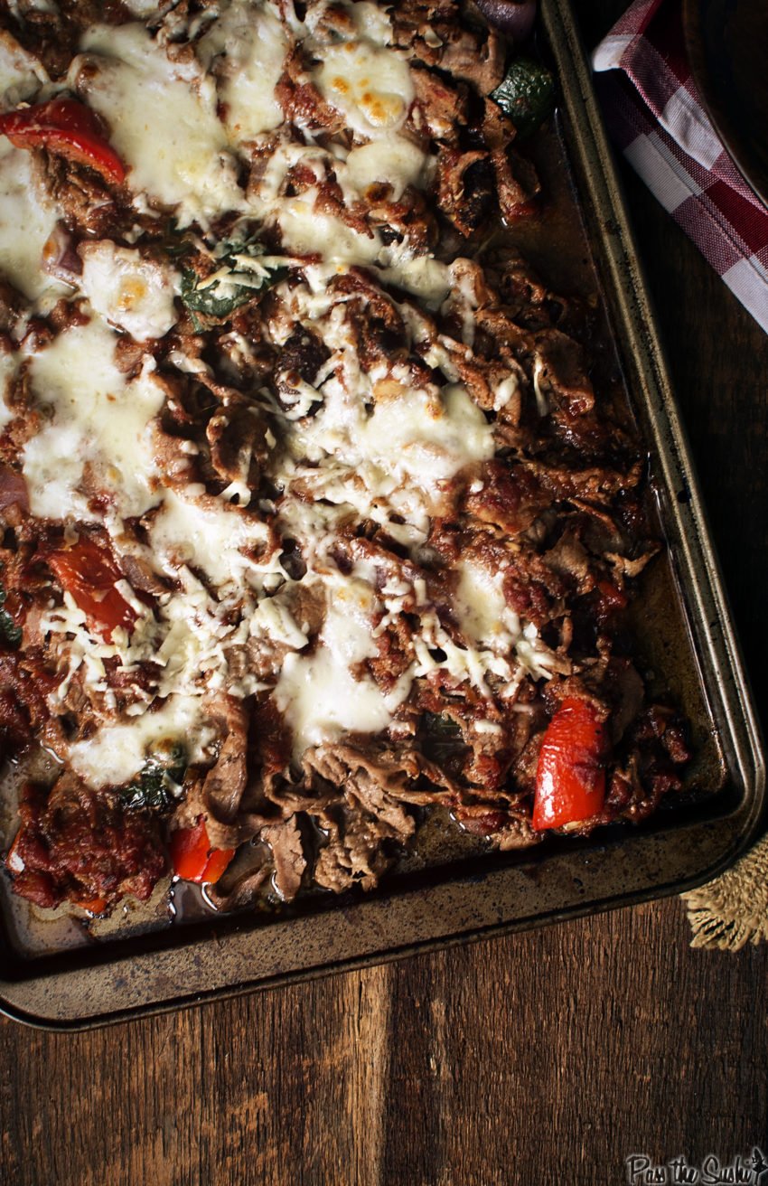 Sheet pan filled with thin shaved steak, roasted veggies and melted cheese. 