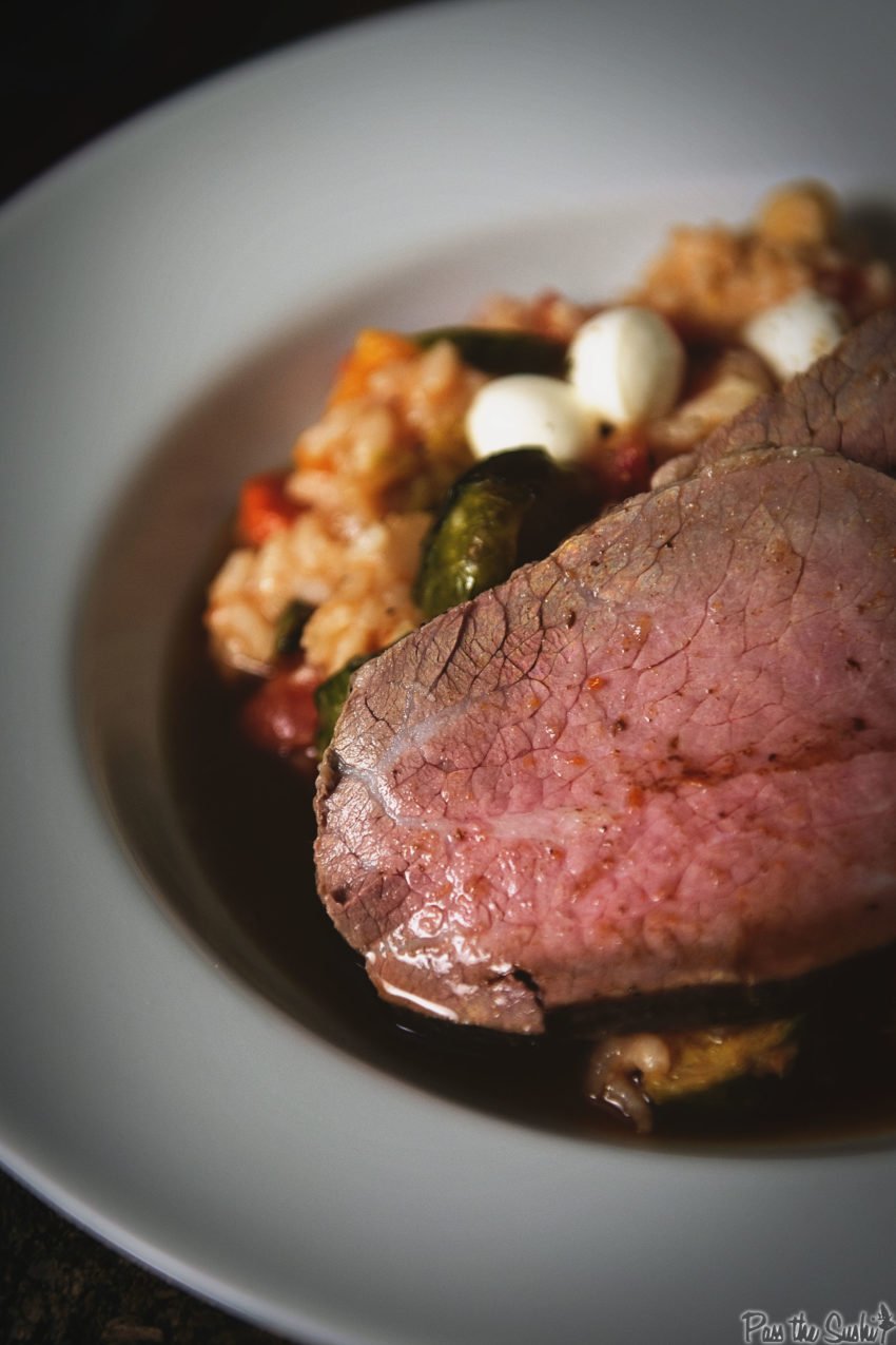 Sliced eye round roast on a white platter over risotto 