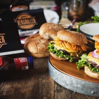 Barbecue burgers with a bottle of bbq sauce on a wooden table.