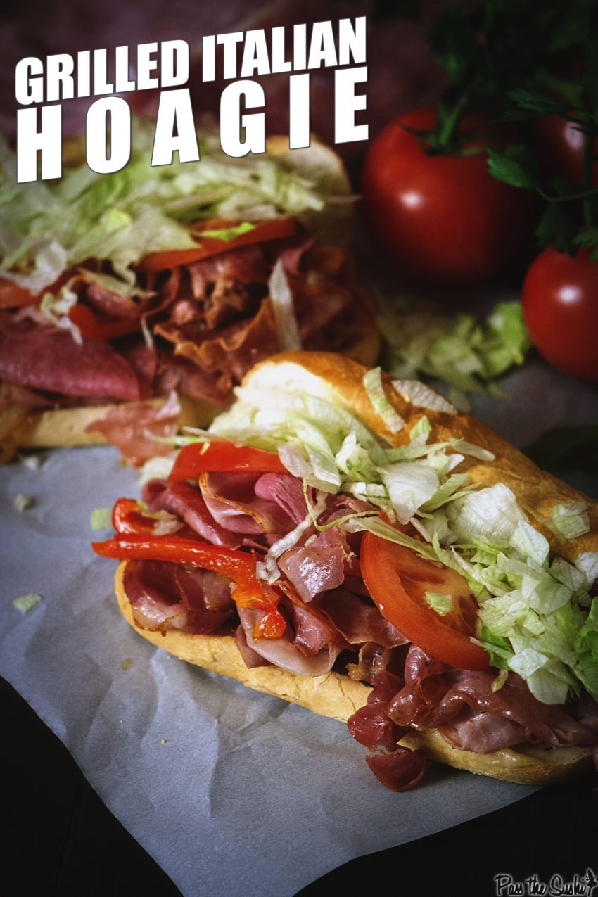 Close up of italian hoagies overflowing with grilled meats, sliced tomatoes, and chopped lettuce. 