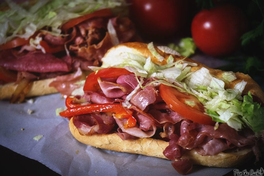 Close up shot of a hoagie roll filled with italian cured meats and sliced tomato and lettuce. 