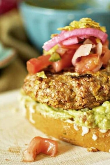 A chicken burger with guacamole and tomatoes.