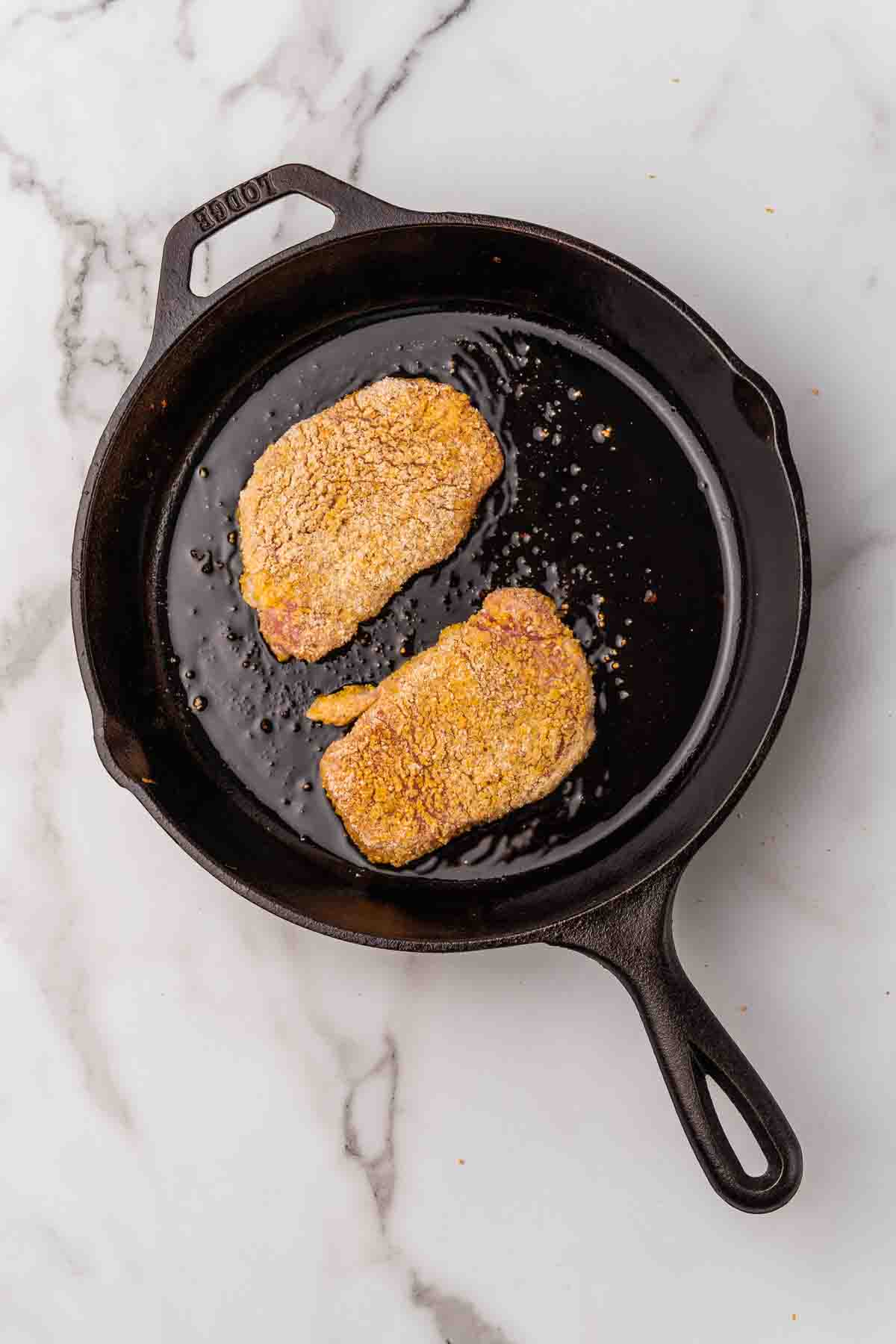 Two pieces of cornmeal-coated chicken in a cast iron skillet.