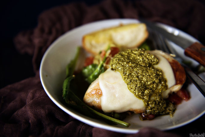 A simple chicken breast covered gently in mozzarella and basil pesto. It's all laid out on a bed of greens, and ready for the table.