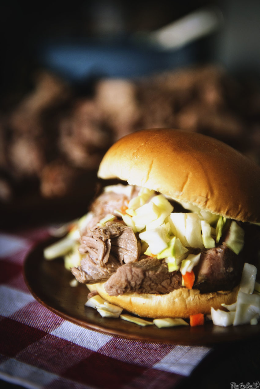 Smoked pulled pork piled into a sandwich with slaw on a red check napkin.