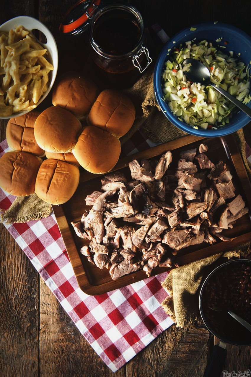 Overhead shot of table with smoked pulled pork, buns, slaw and mac and cheese. 