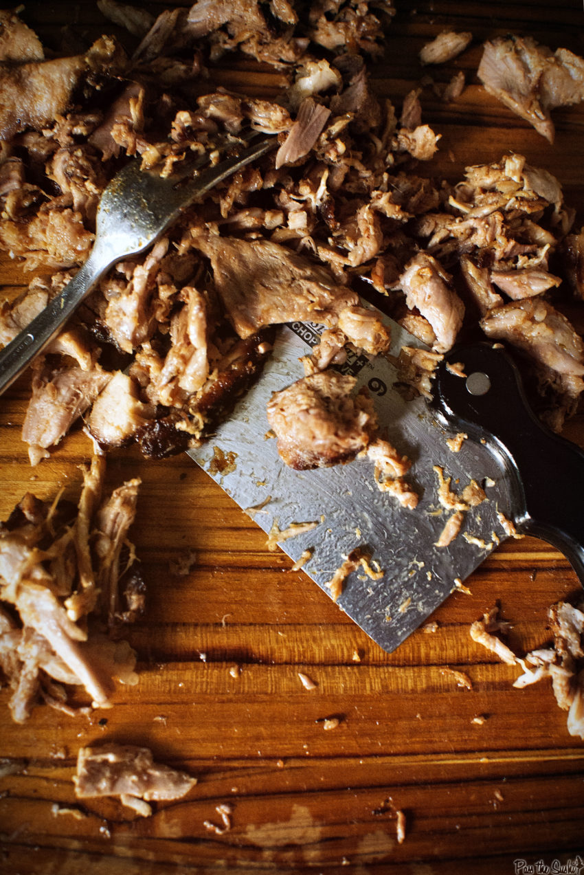 Shredded Smoked Pork a cleaver and a fork on a beautifully grained cutting board. 
