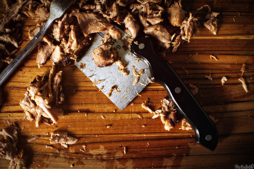 Overhead shot of fork and clever on cutting board with pulled pork all around.