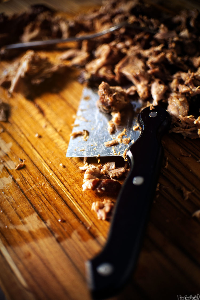 Close up of the handle of a knife in a pile of pulled pork.