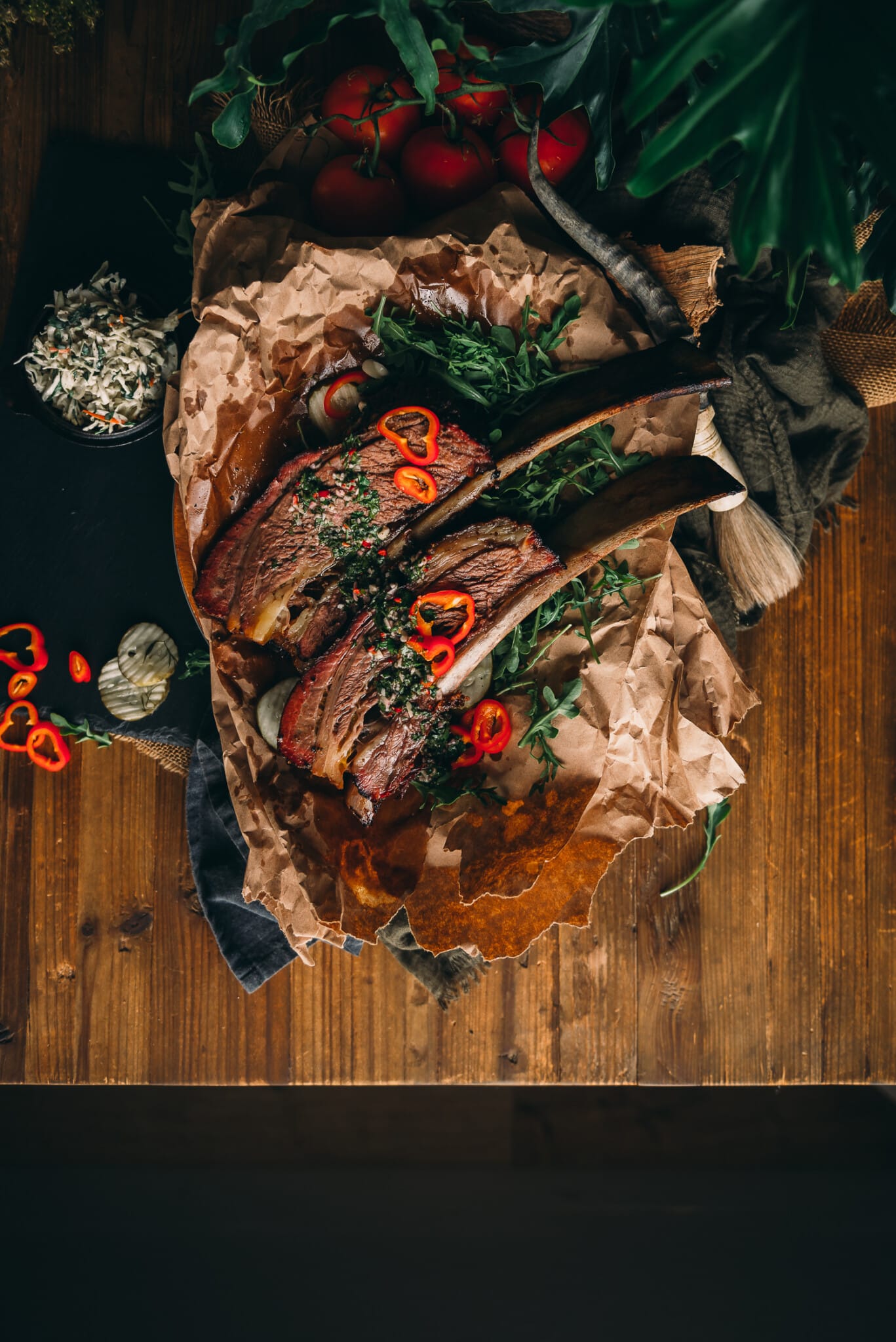 Above shot of 2 bone in giant beef ribs, garnished with chimichurri and sliced peppers. 