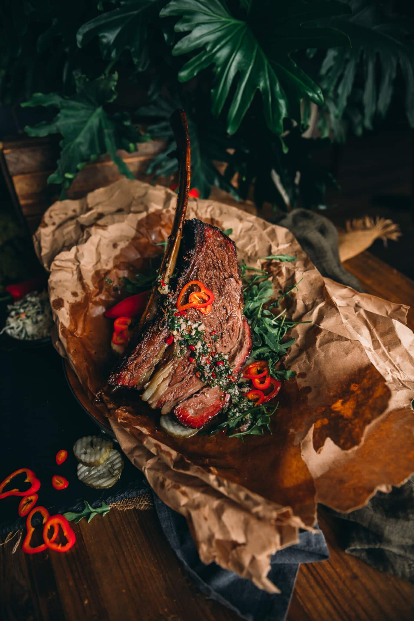 Huge beef rib that's been smoked on crumpled paper and garnished with arugula, peppers, pickles and chimichurri. 