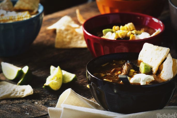 Three bowls filled with glorious Chicken Tortilla Soup, with loads of limes, veggies, tortilla chips and sour cream to go around!