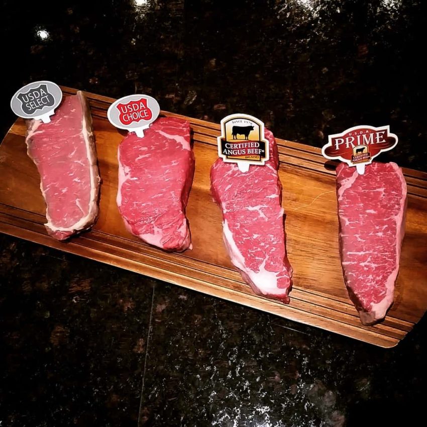Four steaks on a wooden cutting board.