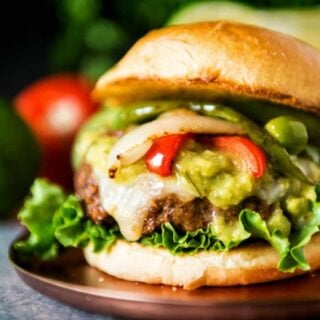 Fajita-inspired burger with guacamole and peppers on a plate.