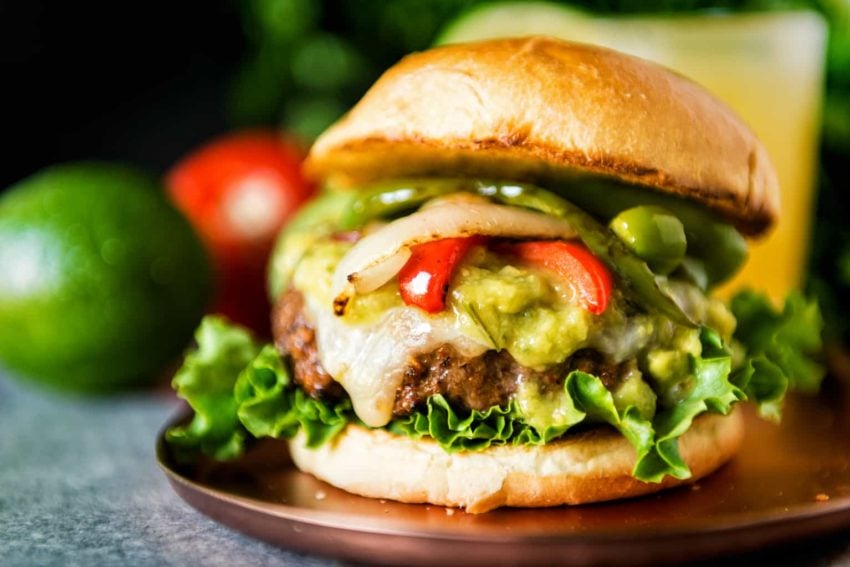 Beautiful vibrant shot of a grilled burger patty on a bun with grilled peppers and onions and a sauce. 