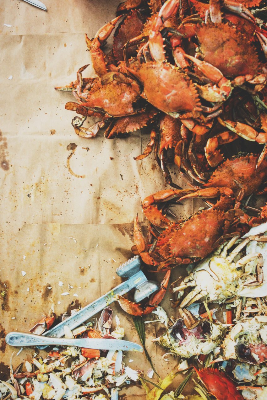 Steamed blue crabs covered in old bay seasoning on a table lined with paper.