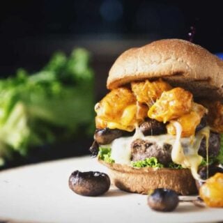 A spud muffin burger with mushrooms and cheese on a wooden plate.