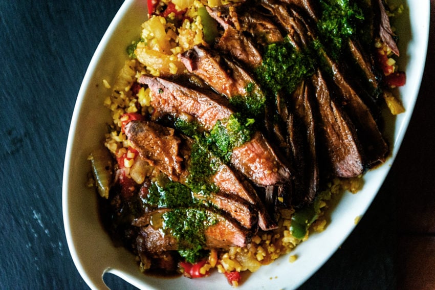 Sliced flank steak with chimichurri drizzled overtop.