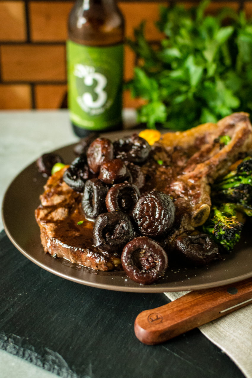 A steak is piled with mushrooms, red wine pan sauce, and laid over a bed of broccoli. 