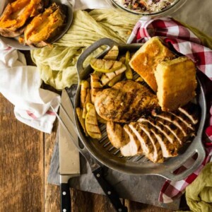 Grilled chicken, cornbread, and roasted vegetables on a tray with a side of coleslaw and baked sweet potatoes.