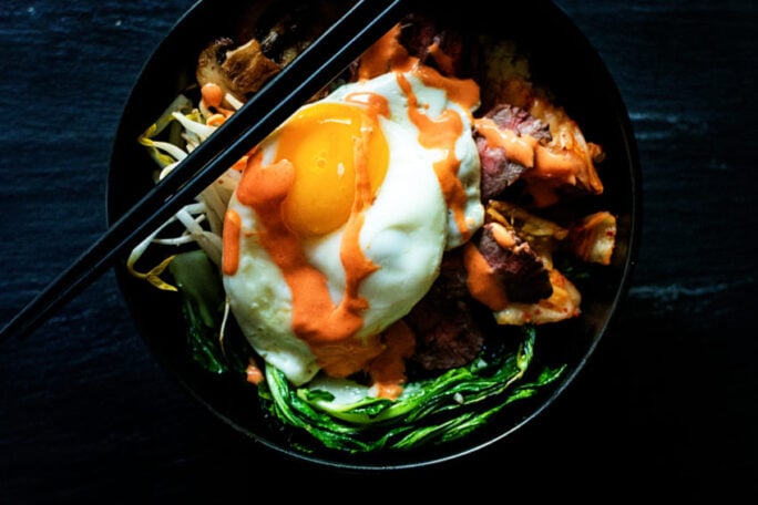 The colors of this steak bibimbap bowl are amazing. red steak, green veggies, yellow yolk, all criss crossed in an orange sriracha mix. Eat the rainbow.