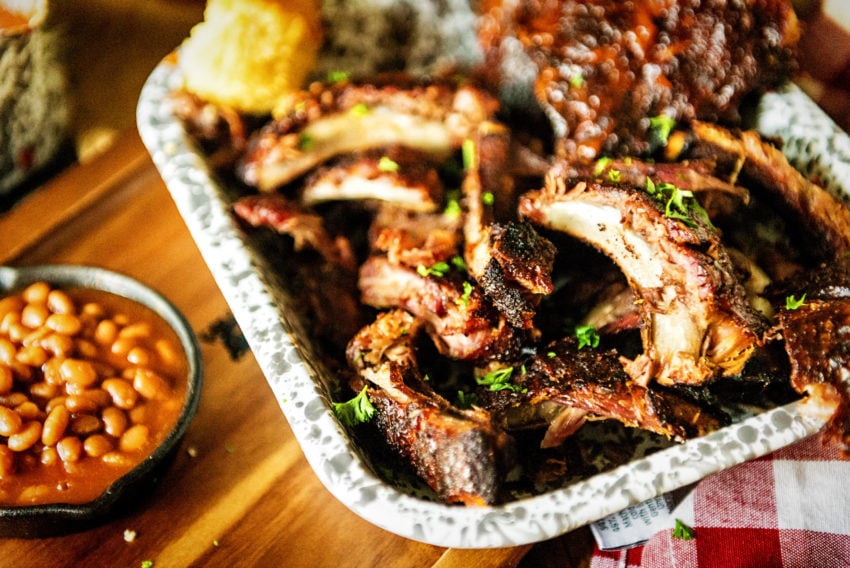 Rack of ribs sliced and piled in a serving platter garnished with parsley and baked beans on the side. 