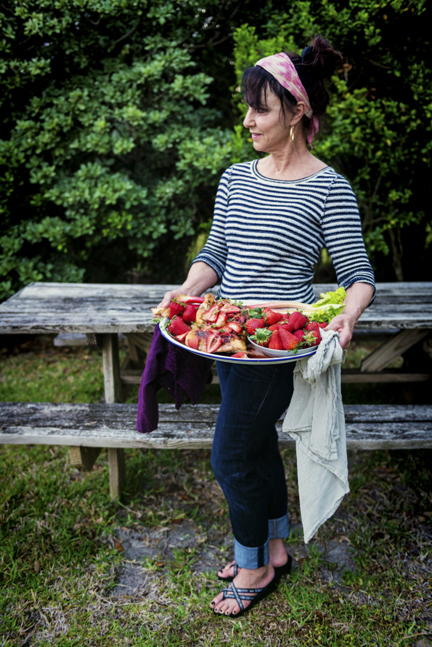 Woman holding platter of roasted chicken, berries and rhubarb. 