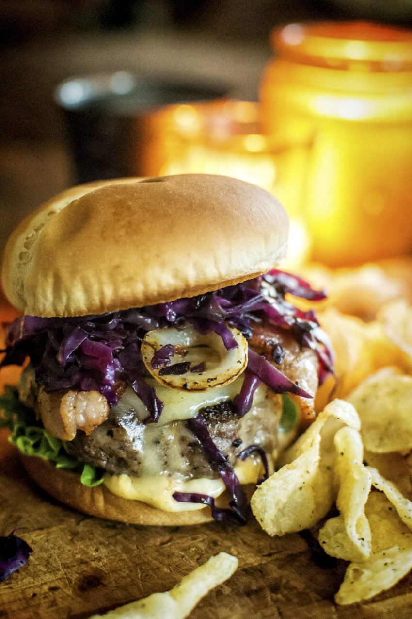 Close up of a thick brat burger with braised red cabbage and chips