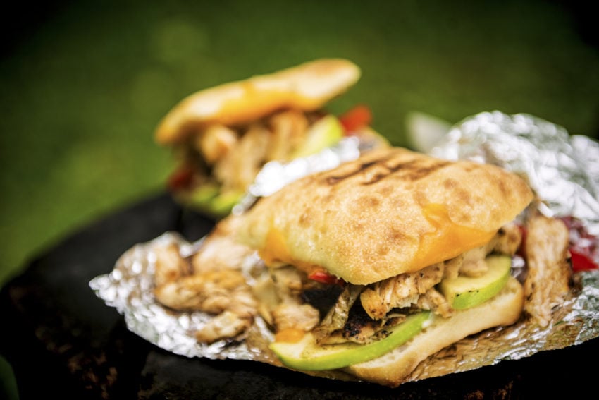Grilled chicken sandwich unwrapped from foil to show melted cheese, chicken and apples. 