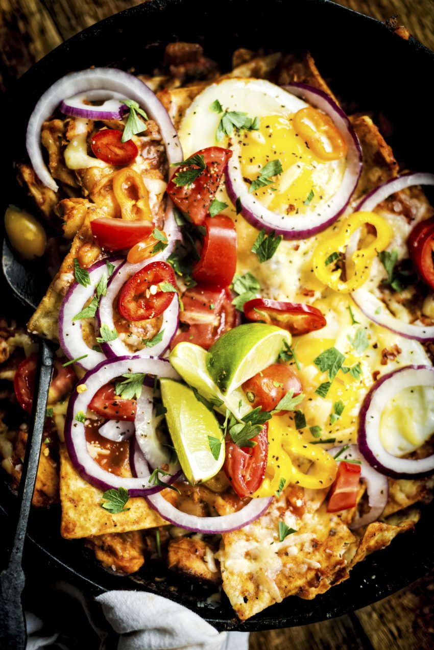 Smoked Chicken Chilaquiles breakfast recipe in a cast iron skillet topped with tomatoes limes and slices of red onion.