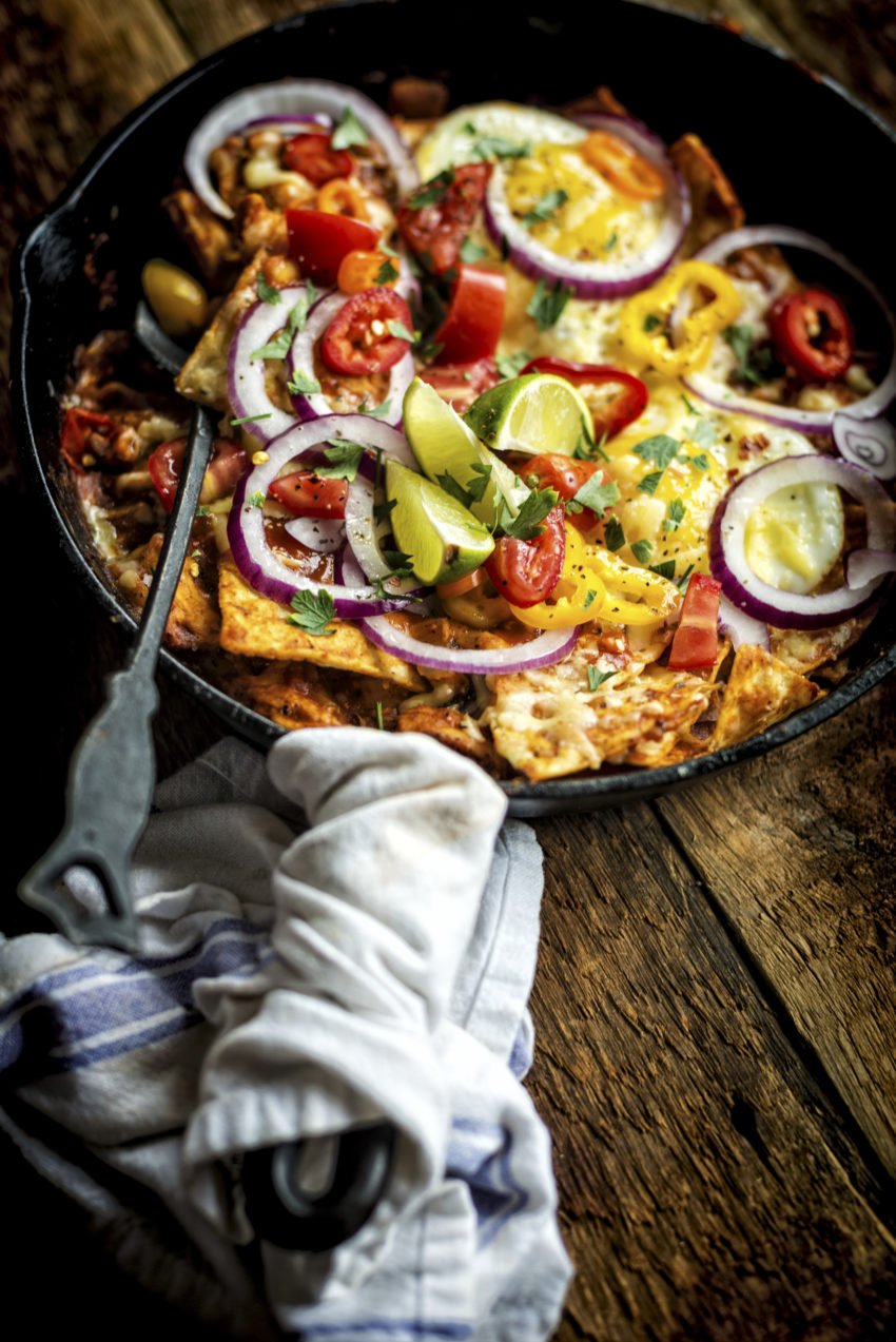 Skillet of chilaquiles topped with tomatoes, red onion slices and lime wedges. 
