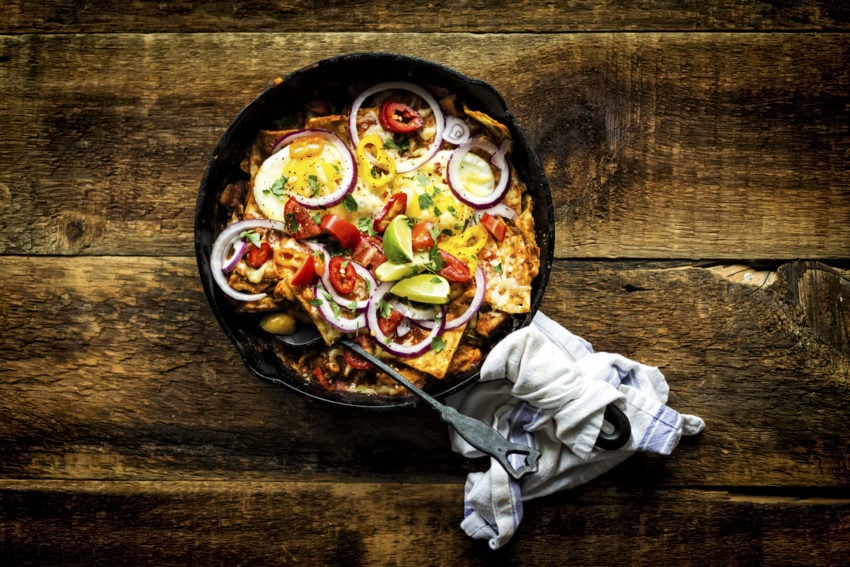 A hearty Smoked Chicken Chilaquiles breakfast in cast iron with fried eggs on top waiting to be devoured.