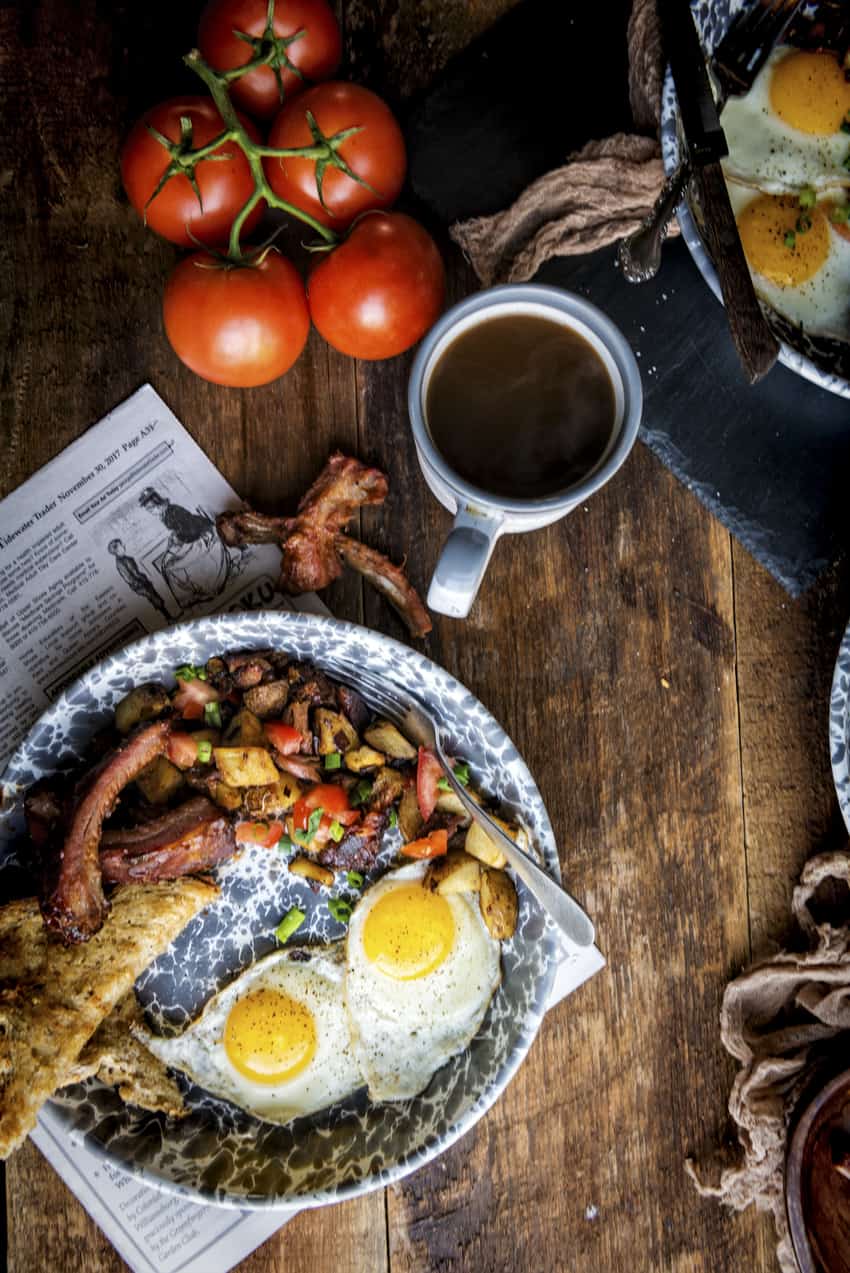 Breakfast scene with coffee and a hearty plate of fried eggs, toast and leftover hash with onions and peppers