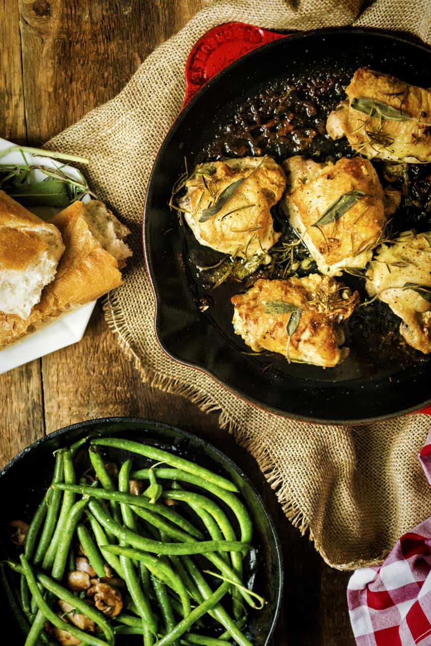 finished pan seared chicken thighs with crispy skin in red pan with herbs