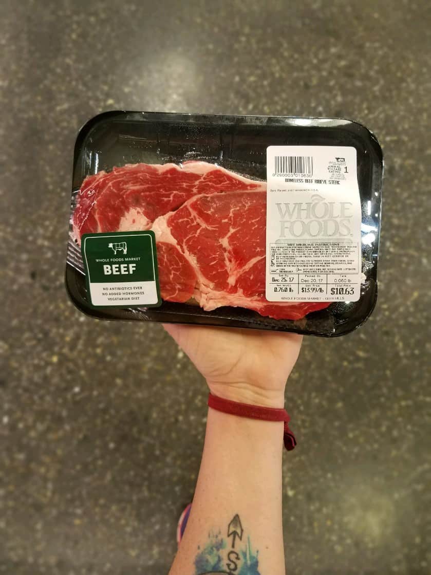 A person displaying a meat label on a piece of steak in a plastic container.