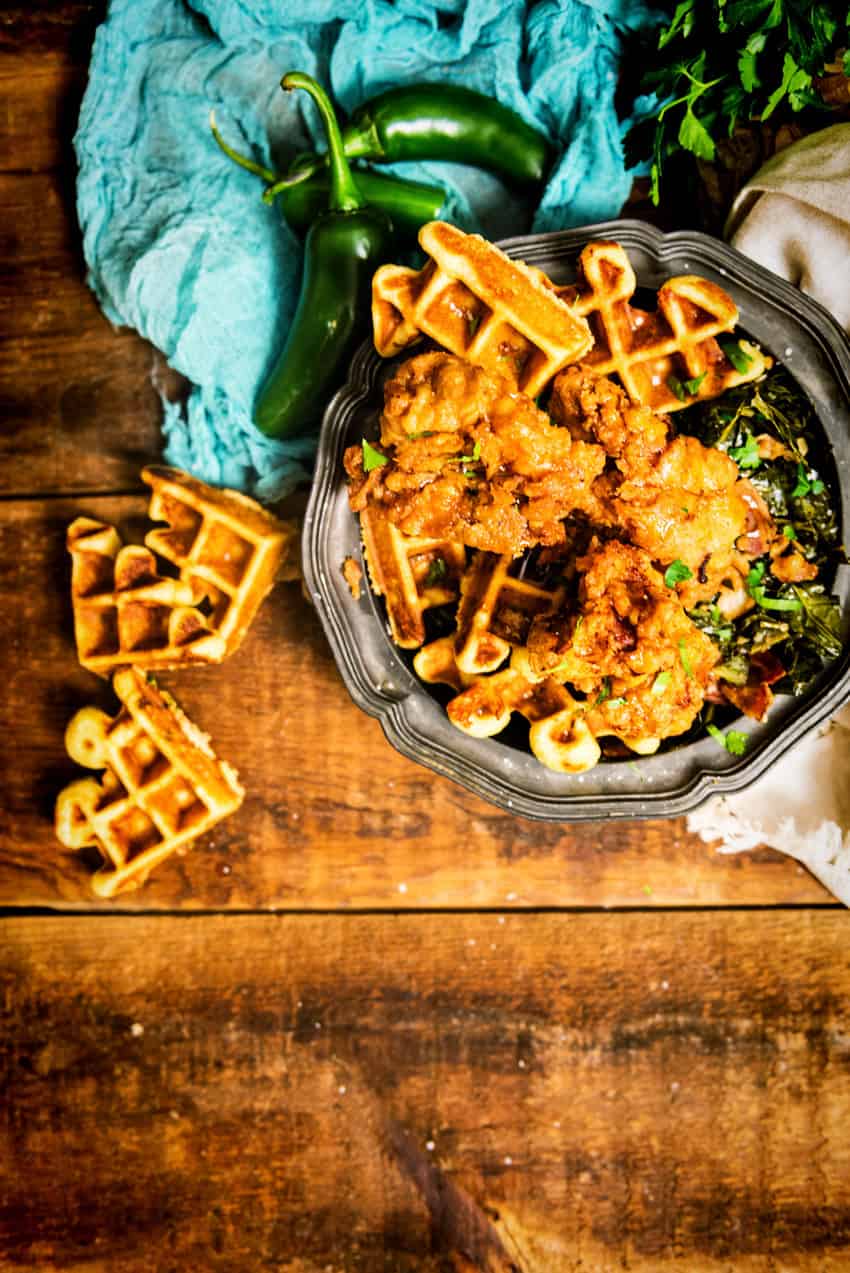 Overhead shot of chicken on aplatter with waffles all on a rustic table. 