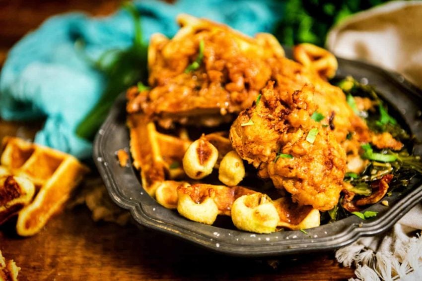 Platter of crispy fried chicken over cornbread waffles with collard greens. 